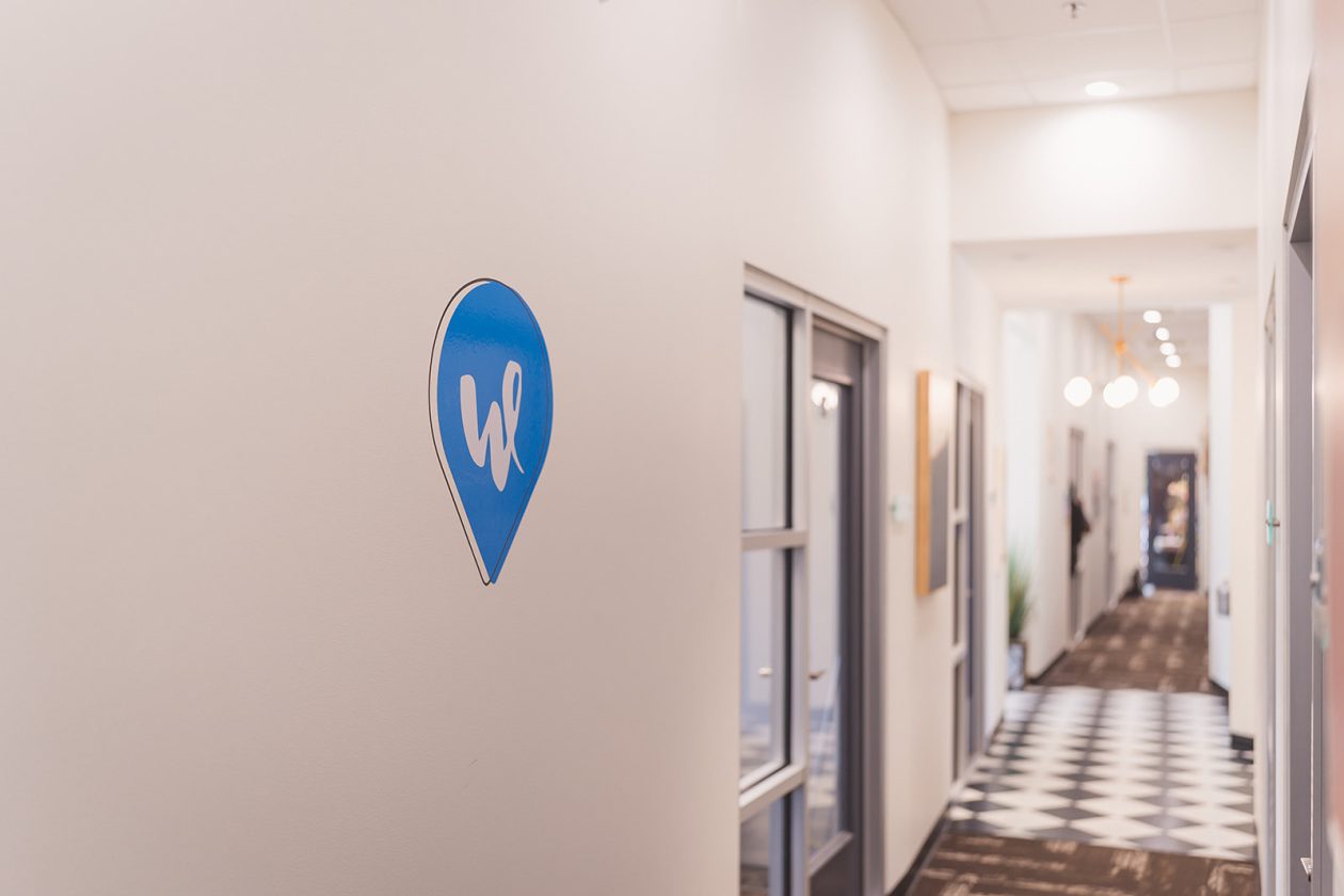 WanderLux pin logo on the wall at the Southpoint location with suites down the hallway